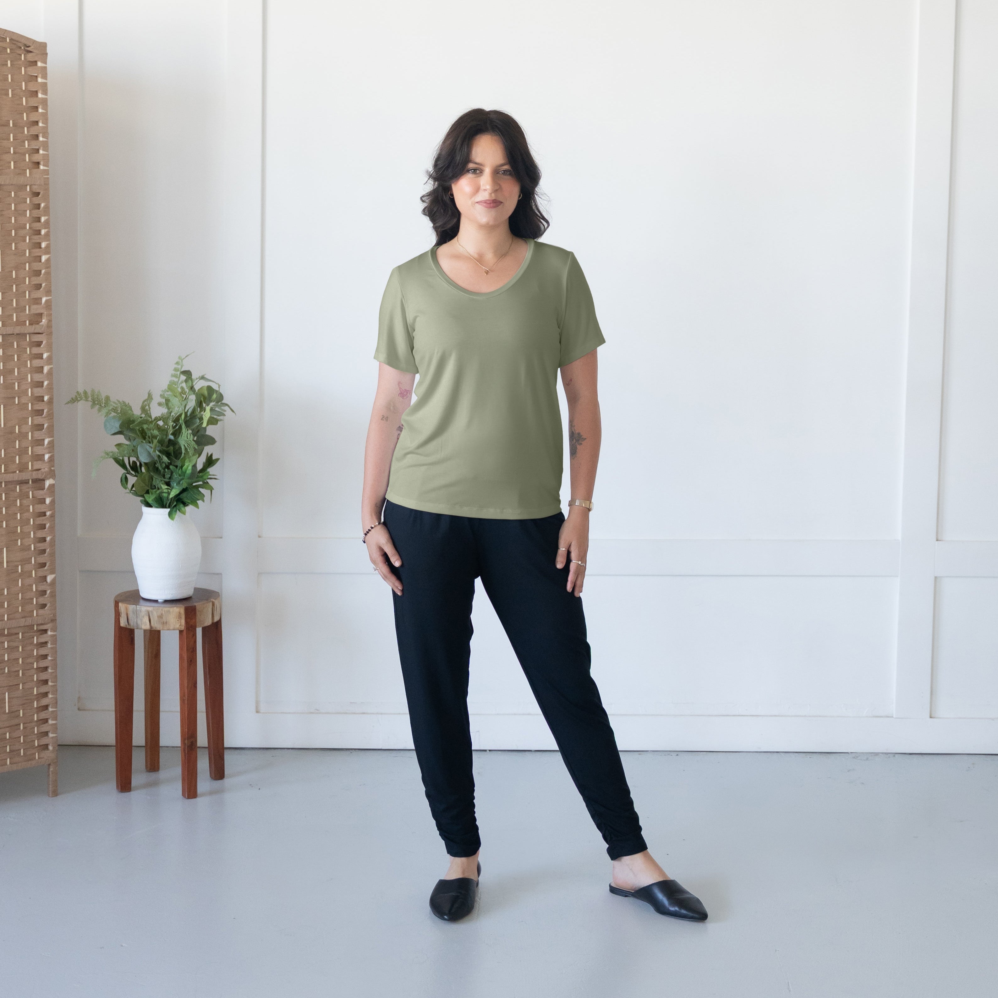 Woman wearing a green t-shirt and black pants standing in a minimalistic room.