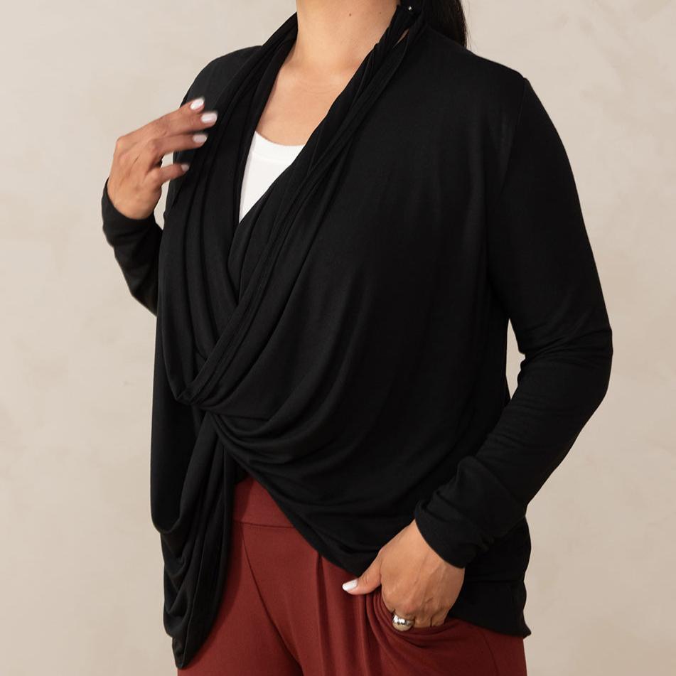 Woman wearing long sleeve black cardigan twisted at the front with white v-neckline shirt and red relaxed pants