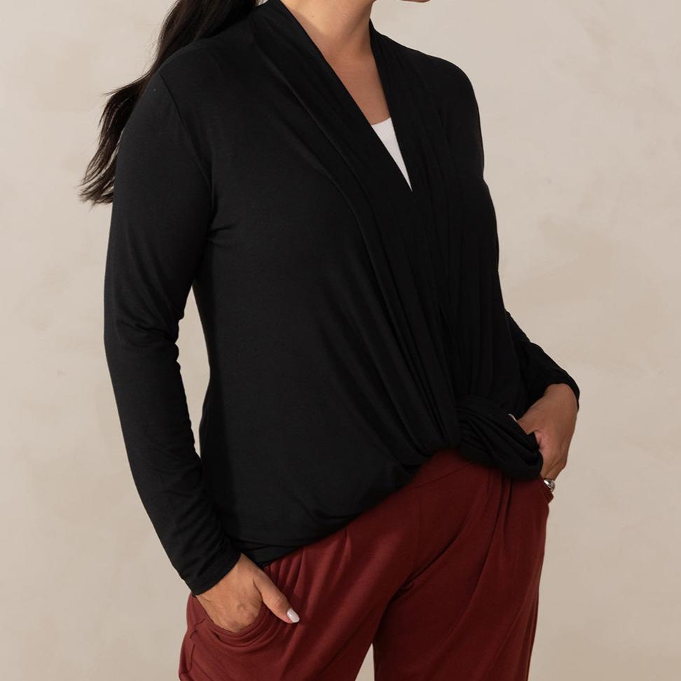 Woman wearing long sleeve black cardigan twisted at the front with white v-neckline shirt and red relaxed pants