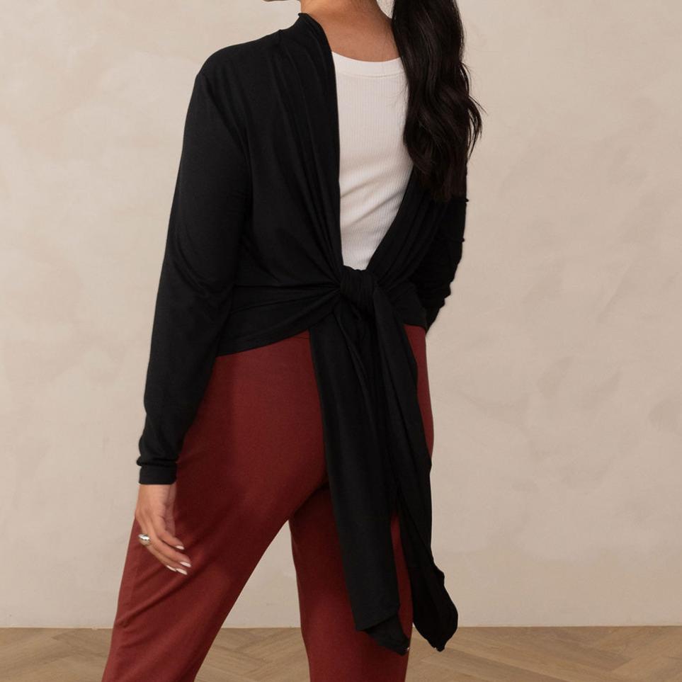 Woman wearing long sleeve black cardigan knotted at the back with white v-neckline shirt and red relaxed pants