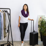 Woman holding a black suitcase next to a rack of clothes in a room.