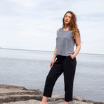 Woman standing on rocks by a body of water wearing a gray tank top and black pants.