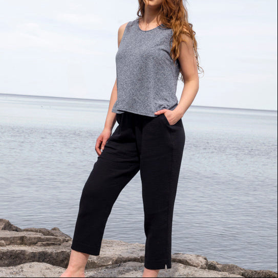 Woman standing on rocks by a body of water wearing a gray tank top and black pants.