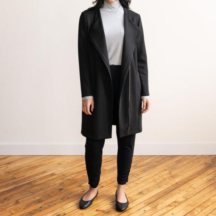 Woman wearing black 3/4 length jacket, light grey turtleneck and black sweatpants