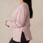 woman wearing a long sleeve scoop neck light pink top paired with tailored grey pants and white sneakers