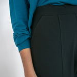Woman wearing black tailored stretchy ankle length pants paired with tucked in teal shirt